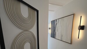 Un couloir avec deux œuvres d’art encadrées accrochées aux murs, un plancher en bois et un interrupteur situé à droite.