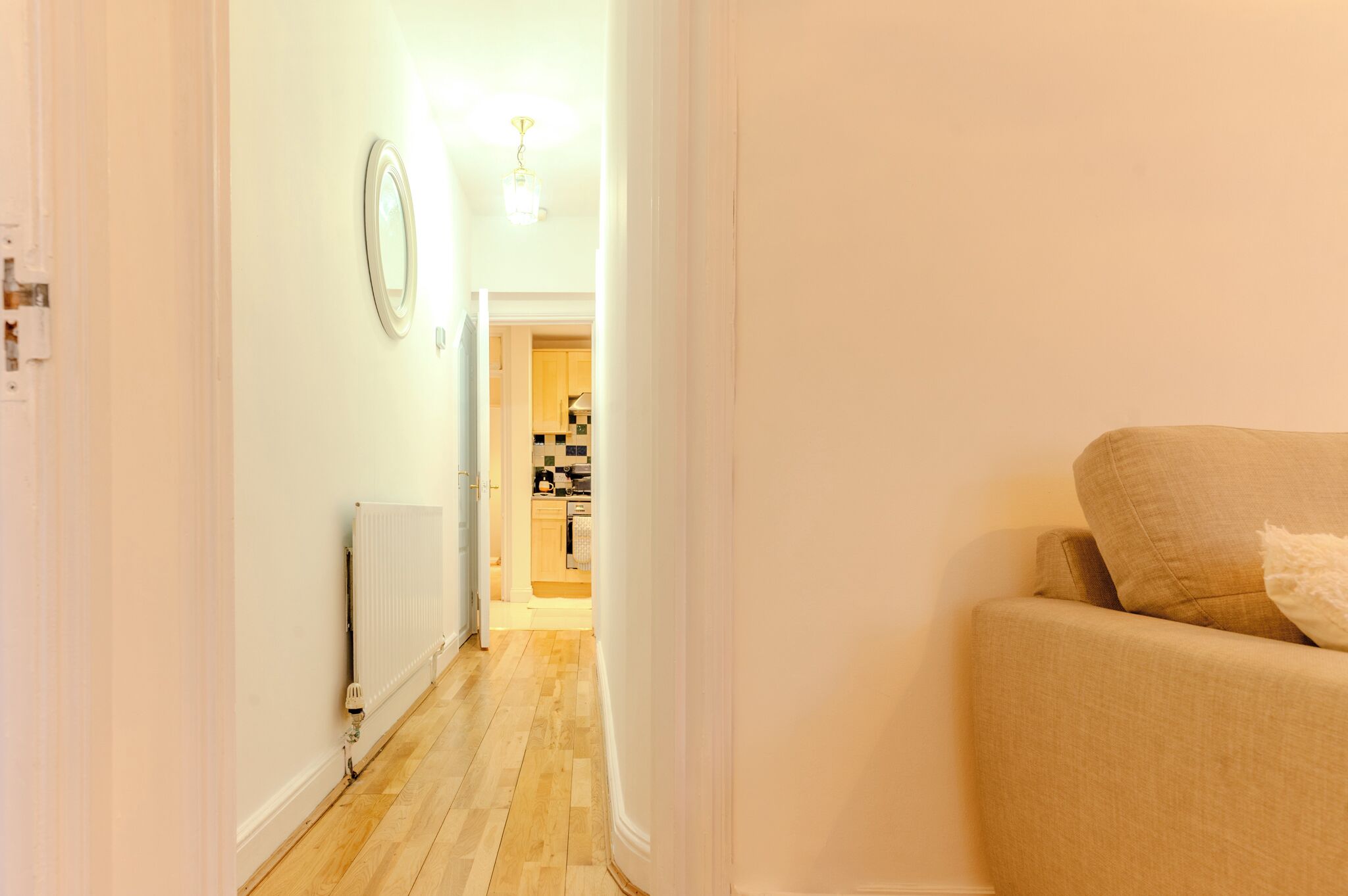 A hallway leading to a kitchen with a radiator, a light fixture, and a beige sofa.