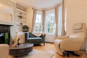 Ein gemütliches Wohnzimmer mit Kamin, einem grünen Sessel, einem beigen Sessel und einem runden Couchtisch.