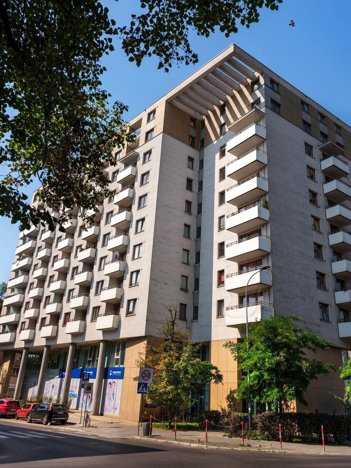 Un immeuble résidentiel à plusieurs étages, doté de balcons, d’une promenade piétonne et d’un espace de stationnement.