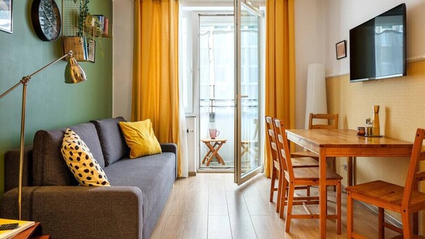 A modern living room with a sofa, a dining table, and chairs. There is a TV mounted on the wall and a window with curtains. - Quiet and well decorated apartment, city heart, Świętokrzyska (Kraków)