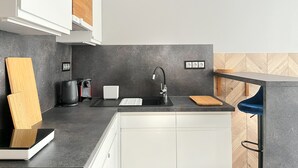 A modern kitchen with a black countertop, white cabinets, a black faucet, and a wooden cutting board. - Comfy studio with projector, Jewish District, Rzeszowska (Kraków)