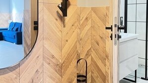 A modern bathroom with a wooden herringbone wall, a black towel rack, and a black trash bin. - Comfy studio with projector, Jewish District, Rzeszowska (Kraków)