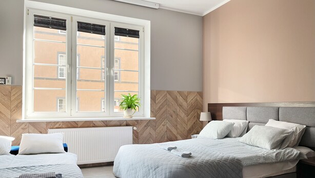 A modern bedroom with two beds, a large window with blinds, a radiator, and a potted plant. - Comfy studio with projector, Jewish District, Rzeszowska (Kraków)