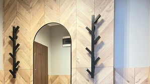 A modern bathroom with a herringbone wood panel wall, a round mirror, a bench, and a black trash bin. - Comfy studio with projector, Jewish District, Rzeszowska (Kraków)