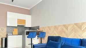 A modern living space with a blue sofa, two blue chairs, a kitchen area, and a herringbone-patterned wall. - Comfy studio with projector, Jewish District, Rzeszowska (Kraków)