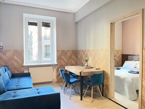 Una habitación compacta con sofá, una mesa de comedor con sillas, cama y ventana con persianas.