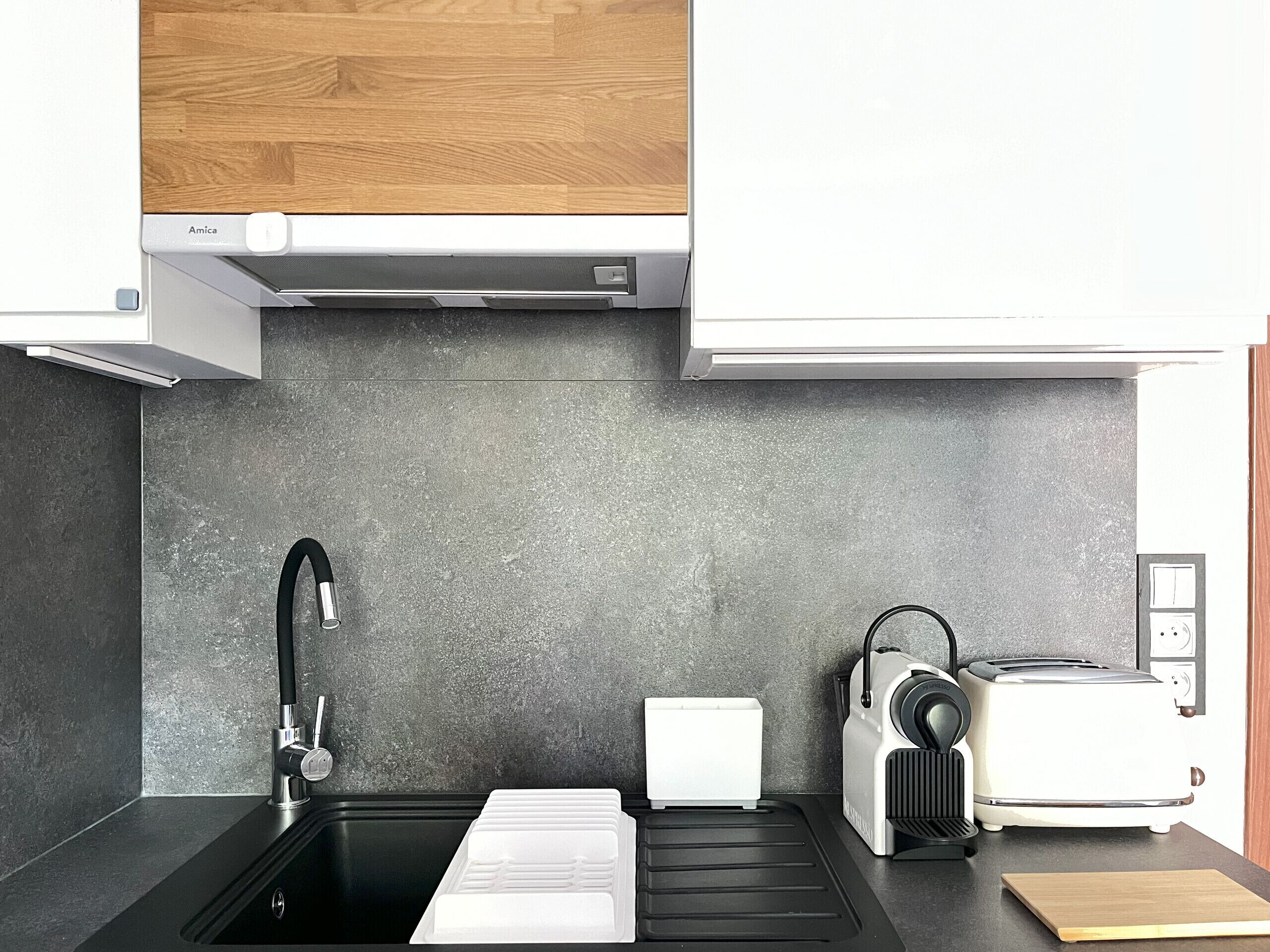 A modern kitchen with a black sink, a white toaster, and a coffee maker.