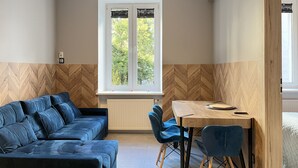 Ein modernes Zimmer mit einer Couch, einem Esstisch und Stühlen. Ein Fenster bietet Blick auf Bäume.
