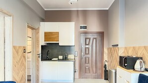 Eine moderne Küche mit weißen Schränken, einer Mikrowelle und einem Toaster. Eine Wand verkleidet mit Holzlatten und eine Tür mit geometrischem Muster.
