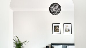 Une chambre moderne avec un parquet en bois disposé en motif chevron, un lit noir, une table de chevet avec une lampe et deux tableaux encadrés accrochés au mur.