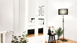 Una habitación con un armario blanco, una lámpara de pie negra, una mesita con una planta y un radiador.