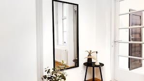 Habitación de esquina con un espejo grande, una mesita con un florero y una lámpara, y piso de madera con motivo de espiga.