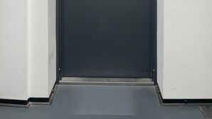 Una puerta negra con un pequeño letrero encima, un timbre y una placa con el número 12.