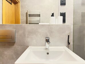 Une salle de bain moderne avec un lavabo blanc, un porte-serviettes et des articles de toilette rangés sur une étagère.