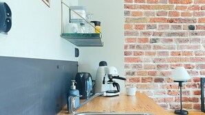Una cocina moderna con pared de ladrillo, máquina de café, hervidor y un cartel que dice 'FOOD IS GOOD WINE IS BETTER'.