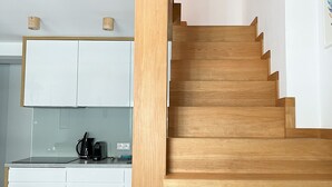 A modern interior with a wooden staircase, a kitchen area with white cabinets, and a built-in seating area with cushions.