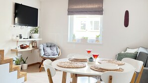 A modern living room with a dining area, featuring a flat-screen TV, a comfortable sofa, and a dining table set for four.