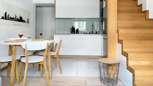 A modern kitchen with white cabinets, a dining area with a round table and wooden chairs, and a staircase with wooden steps.