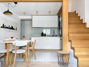 Una cucina moderna con mobili bianchi, un'area pranzo con tavolo rotondo e sedie in legno, e una scala con gradini in legno.