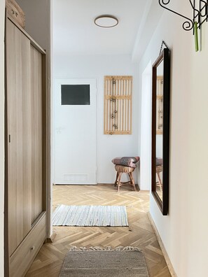 Ein Flur mit einem Holzschrank, einer weißen Tür mit kleinem Fenster, einem gewebten Hocker und einem Spiegel an der Wand.