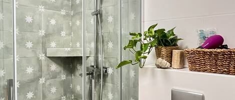 Ducha envuelta en vidrio con pared de azulejos con diseño de estrellas, una bañera blanca y un estante con una planta y artículos de aseo.