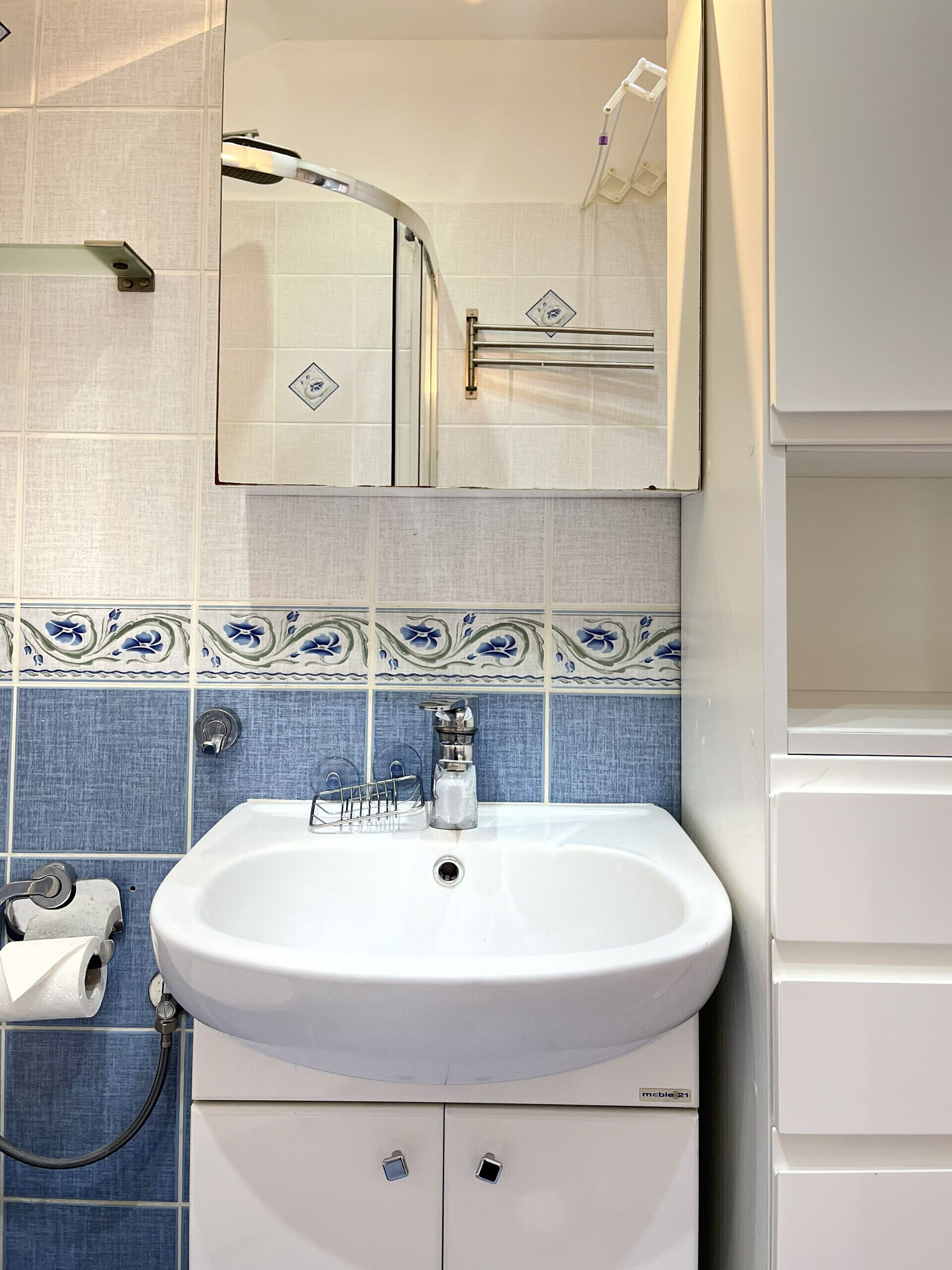 Un baño con un lavamanos blanco, azulejos azules estampados, un espejo y un perchero para toallas.