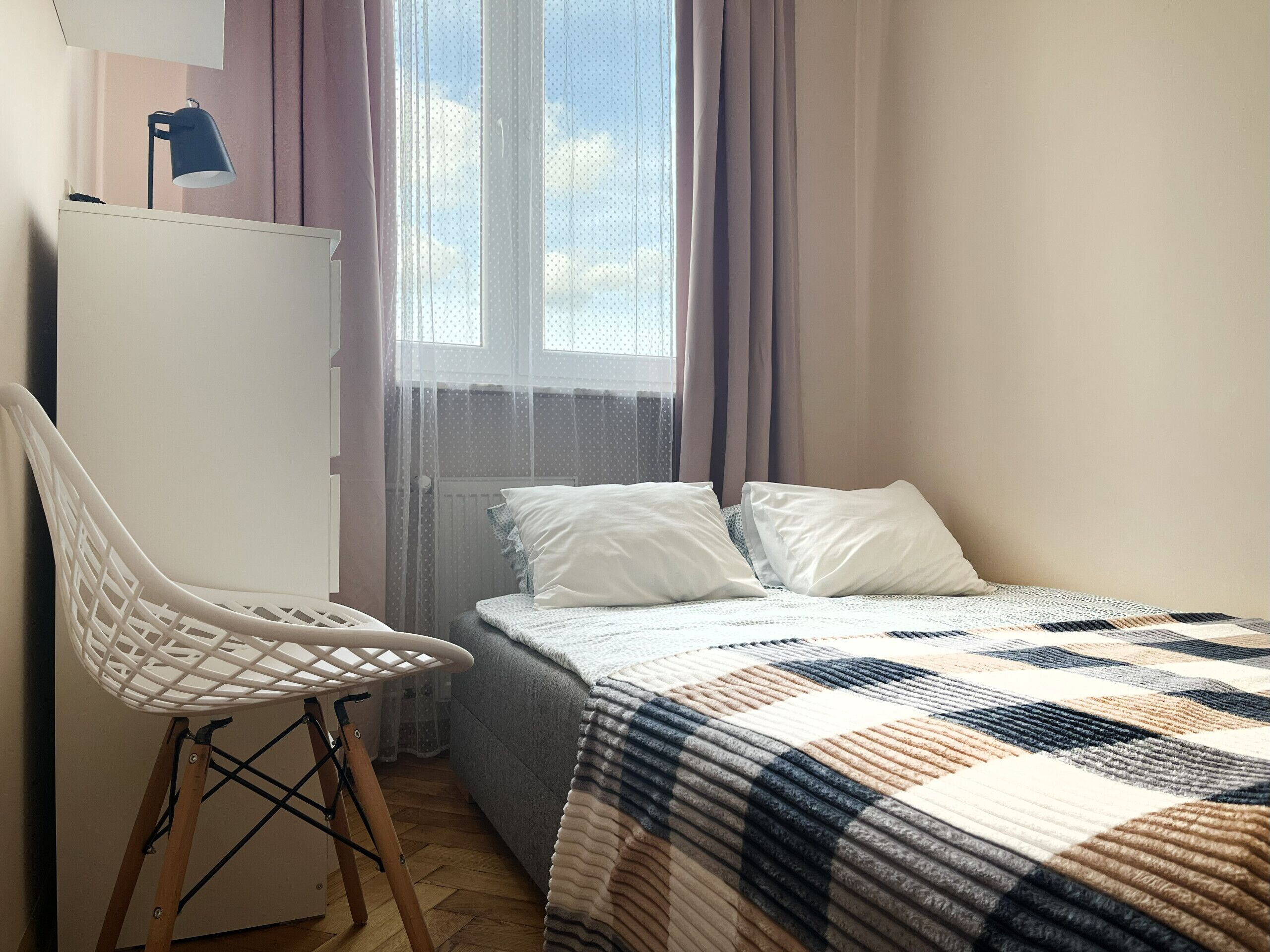 Un dormitorio con cama, una silla, un escritorio y una ventana con cortinas.