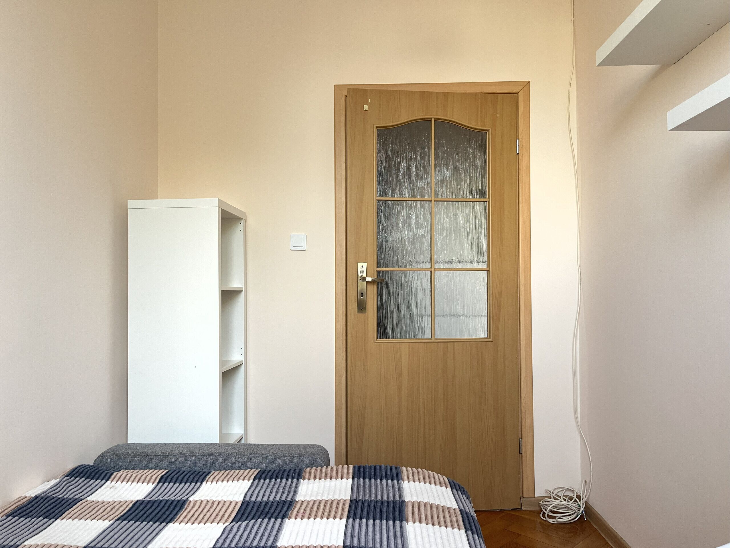A bedroom with a wooden door, a white wardrobe, and a bed with a striped blanket.