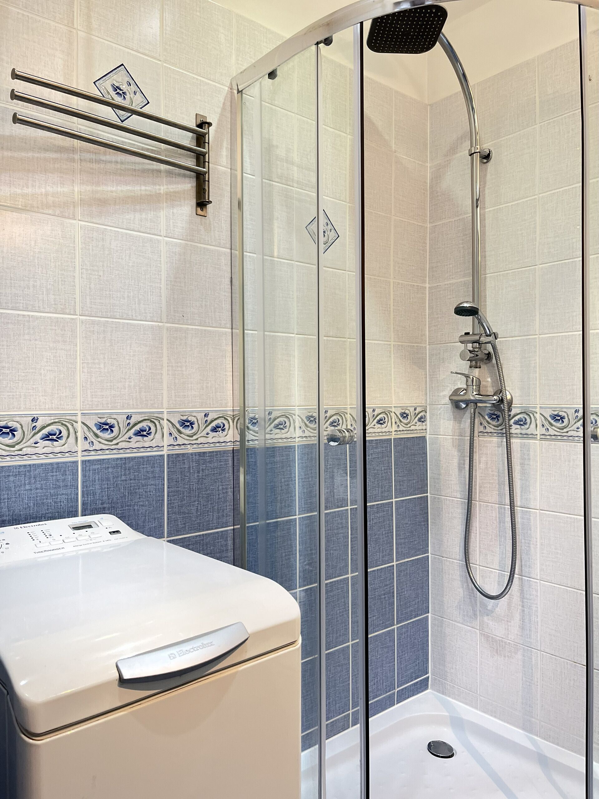 A glass-enclosed shower with a handheld showerhead and a wall-mounted faucet.