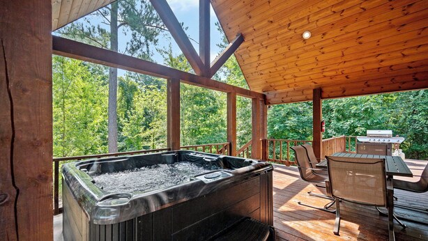 Eine Holzterrasse mit Whirlpool, Sitzgelegenheit und Blick ins Waldgebiet.