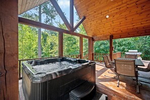 Una terraza de madera con un jacuzzi, asientos al aire libre y vistas al bosque.