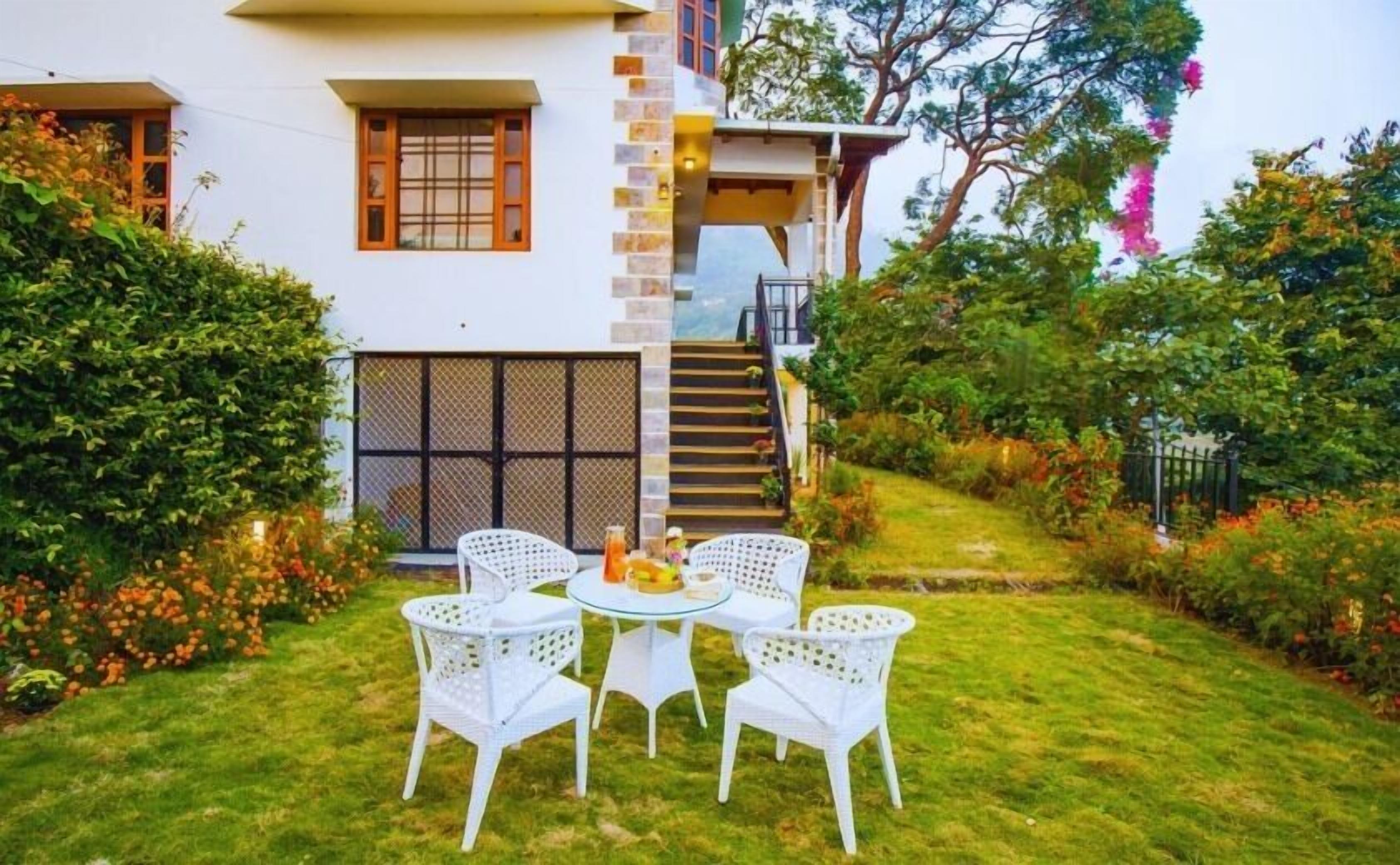 Een woonhuis met twee verdiepingen, een klein balkon, een trap en een tuin met witte stoelen en een tafel.