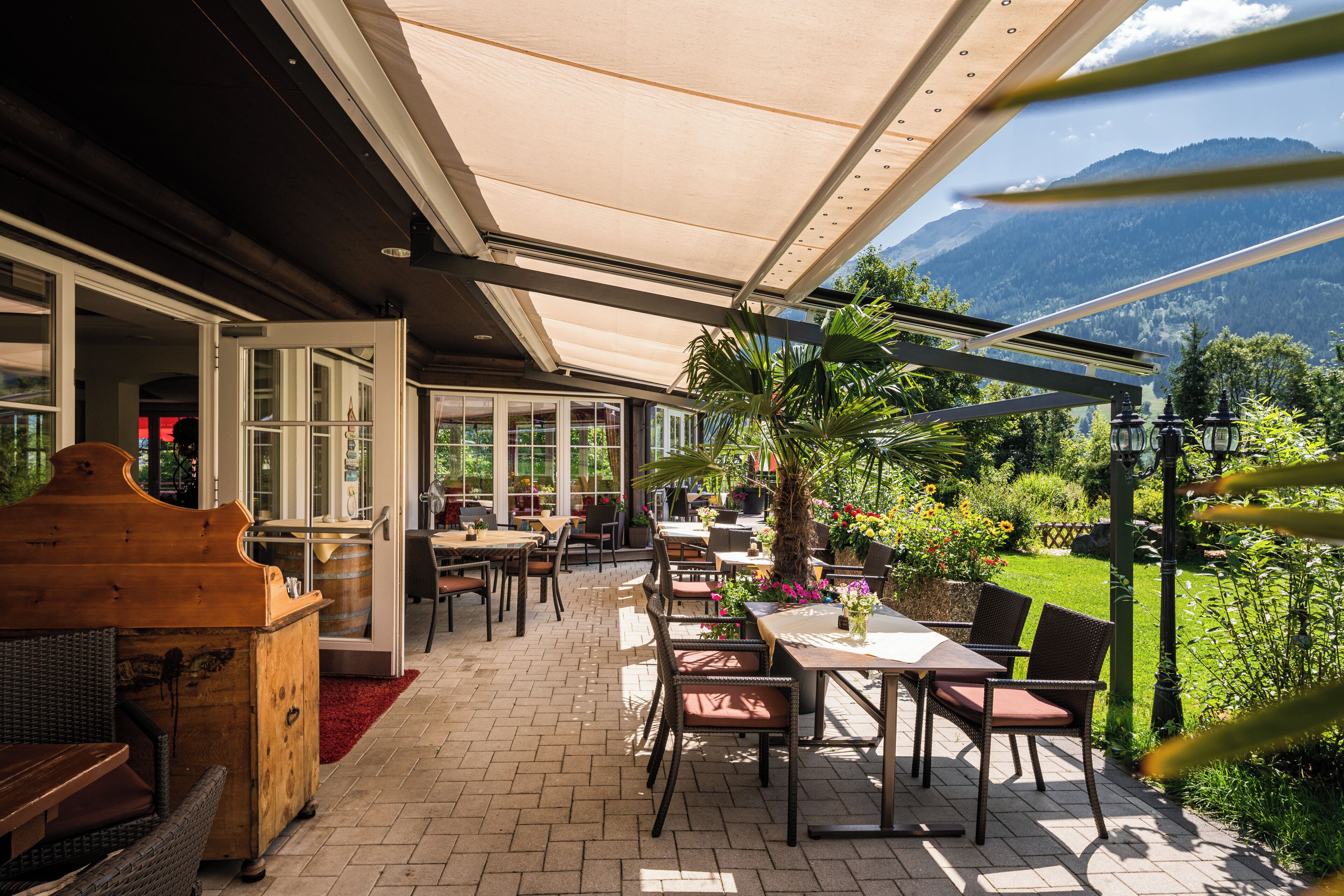 Un patio al aire libre con mesas y sillas, un piano de madera y vistas a las montañas.