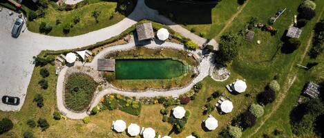 An aerial view of a landscaped area with a central pond, surrounding seating areas, and a building with solar panels.