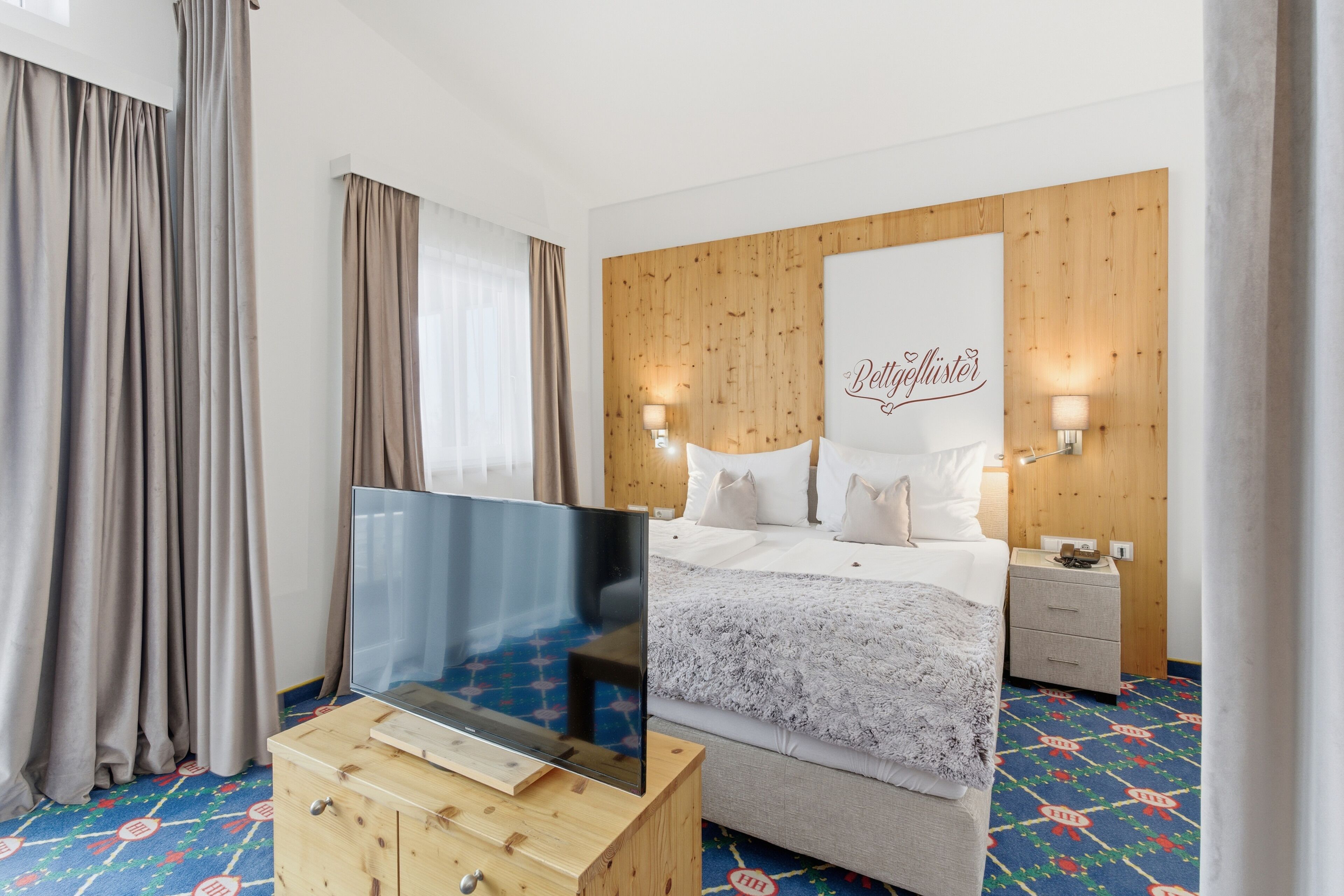 Una camera da letto con un letto, una televisione su un mobile in legno, un comodino e una testiera con una targhetta.
