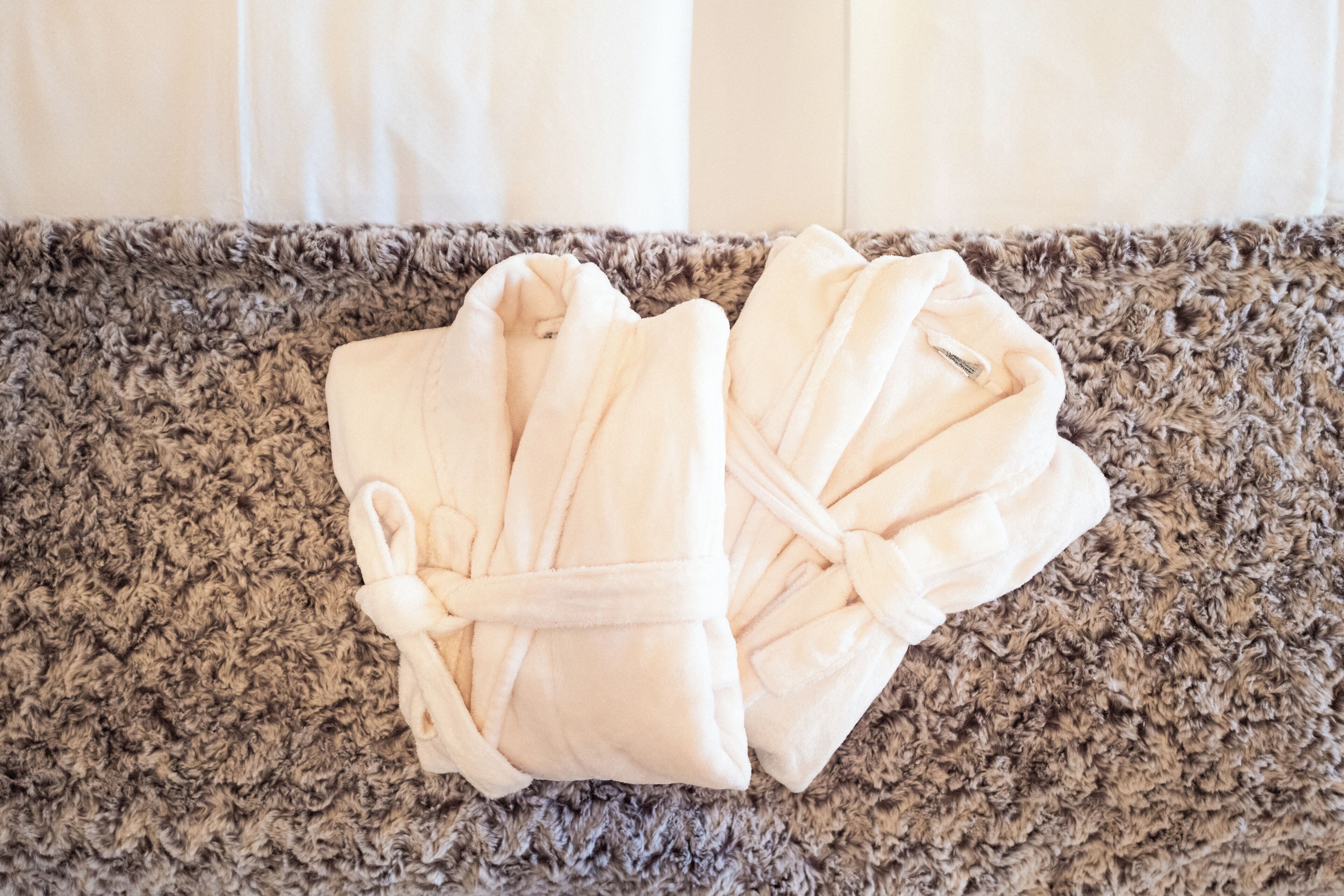 A pair of white bathrobes on a textured carpet.