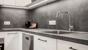 A modern kitchen with white cabinets, a stainless steel sink, and a built-in oven. - EIR Three Bedroom Penthouse (Reykjavík)