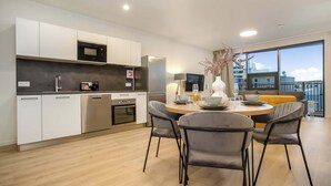 A modern kitchen with white cabinets, stainless steel appliances, and a dining area with a round table and grey chairs. - EIR Two Bedroom Apartments (Reykjavík)