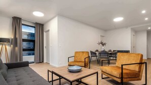 A modern living room with a grey sofa, two armchairs, a coffee table, and a dining area with a table and chairs. - EIR Two Bedroom Apartments (Reykjavík)