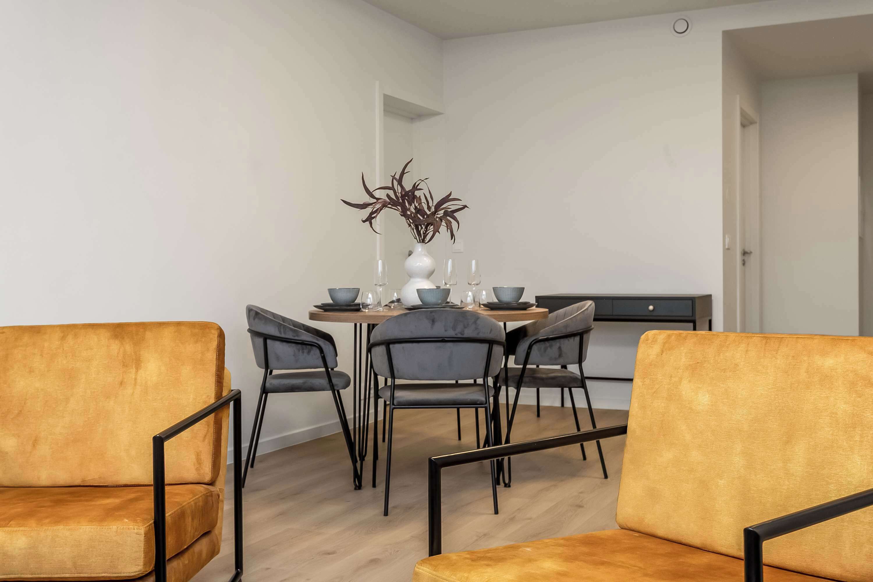 Ein moderner Essbereich mit einem Holztisch, vier grauen Stühlen und einer Vase mit Zimmerpflanzen.