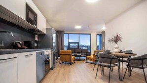 A modern kitchen with a built-in microwave and oven, a dining area with a round table and four chairs, and a large window offering a view of the cityscape. - EIR Two Bedroom Apartments (Reykjavík)