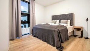 A bedroom with a bed, a nightstand, a window with curtains, and a view of the outside. - EIR Two Bedroom Apartments (Reykjavík)