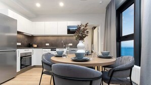 Una cocina moderna con armarios blancos, un refrigerador de acero inoxidable y un comedor con una mesa redonda y sillas grises.