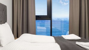 Habitación de hotel con un ventanal grande que ofrece vistas a un cuerpo de agua y montañas.