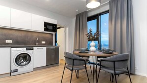 Una cocina moderna con lavadora incorporada, un comedor con mesa y sillas, y un ventanal con cortinas.