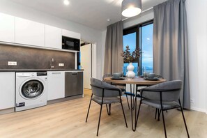 A modern kitchen with a built-in washer, a dining area with a table and chairs, and a large window with curtains. - EIR Two Bedroom Penthouse (Reykjavík)