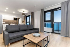 A modern living room with a grey sofa, a wooden coffee table, and a view of the sea through large windows. - EIR Two Bedroom Penthouse (Reykjavík)