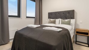 A modern hotel room with a large bed, a bedside table, and a window with curtains. - EIR One Bedroom Apartments (Reykjavík)