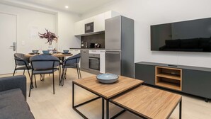 A modern kitchen with a microwave, oven, and refrigerator. There is a dining table with chairs and a bowl on it. A flat-screen TV is mounted on the wall. - EIR One Bedroom Apartments (Reykjavík)